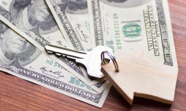 Funding Available Through Local Groups to Help Home Buyers Money with a key and wood house trinket on it