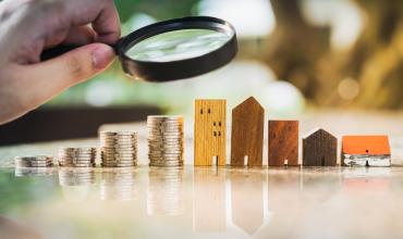 Public Comments Requested a hand holding a magnifying glass over Wooden toy houses