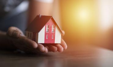 Person holding a small house in their hands over a desk