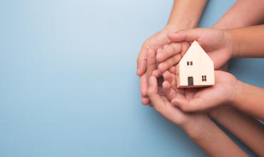 two hands holding a wooden house toy