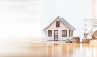 A small model home with coins stacked up next to it