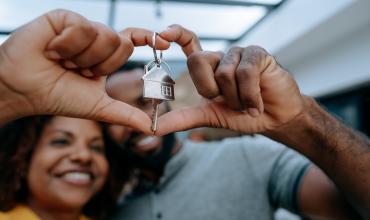 Couple holding up their house keys making a heart shape with their fingers