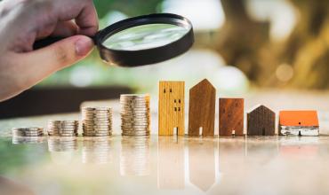 A magnifying glass over a stack of coins and houses