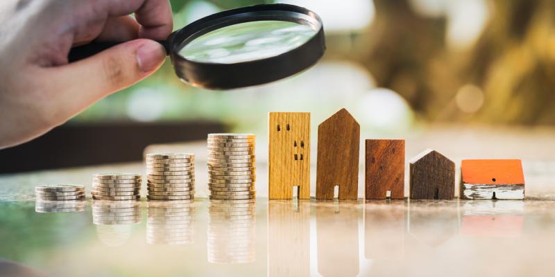 Public Comments Requested a hand holding a magnifying glass over Wooden toy houses