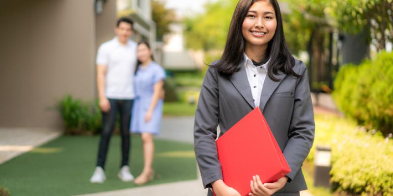 a real estate agent standing in the foreground with a couple standing together in the background