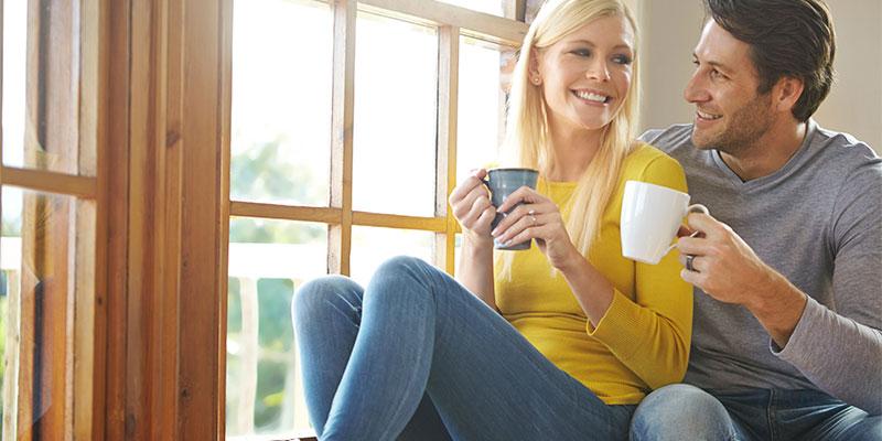 a young couple sitting on a windowsill, smiling and drinking coffee