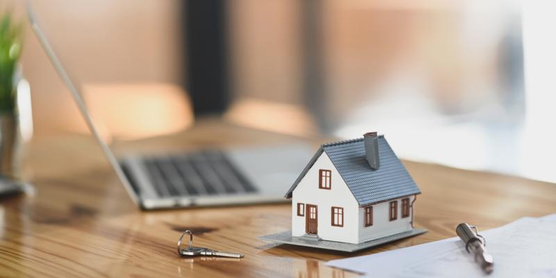 Miniature house beside a keyboard and paperwork on desk