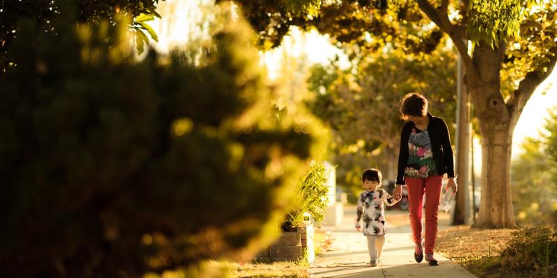 a woman and a boy holding hands walking down a sidewalk