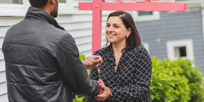 A woman shaking a man's hand in front of a sold sign