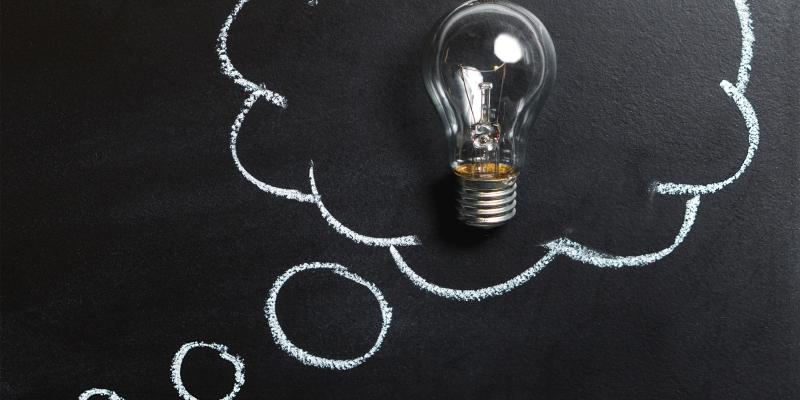 A light bulb in a drawing of a thought cloud on a chalkboard